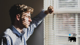 Man looking through window blinds, waiting for his bike to arrive.